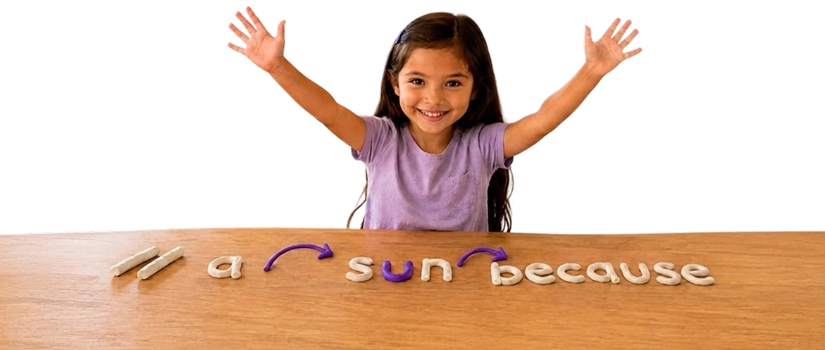 A smiling child raising both hands over a table with clay letters spelling reading practice words