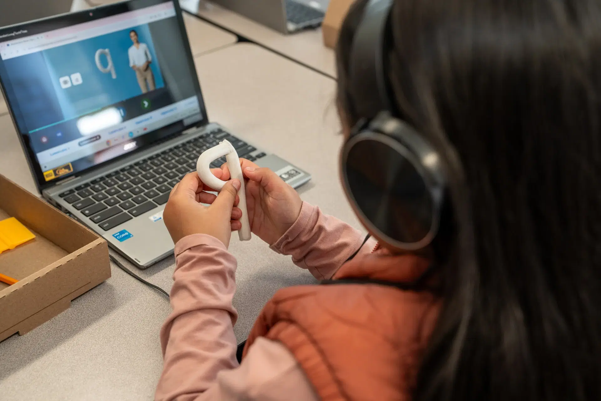 A child works with clay letters and a workbook alongside an adult wearing headphones