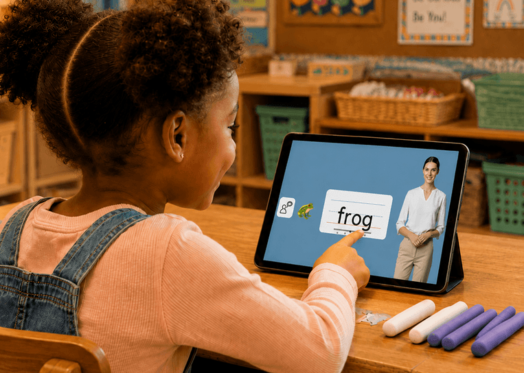 A student pointing at a tablet showing the word ‘frog’, with clay sticks on the desk